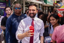Zohran Mamdani smiling while holding a red slushy, in front of other New Yorkers
