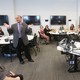 Students and professors sit around tables as one professor speaks. 