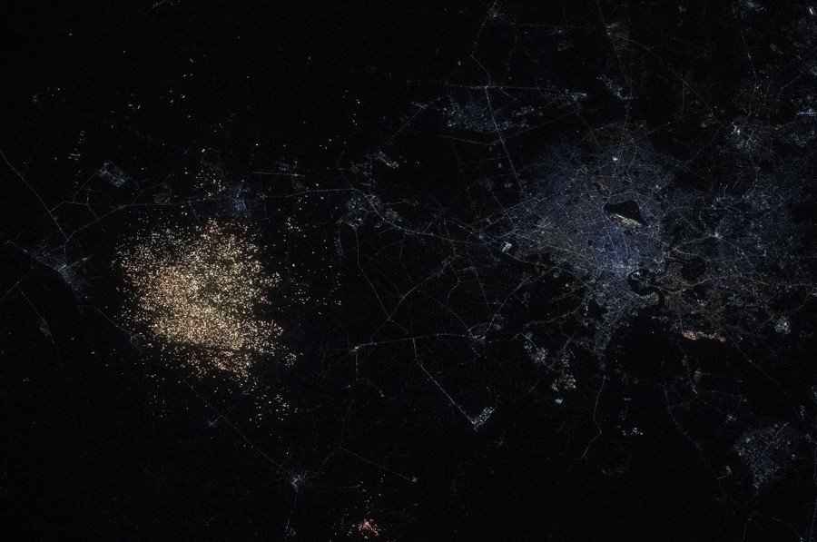 A night view of a city, seen from orbit, alongside a patch of hundreds of small illuminated farm plots