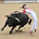 A performer leaps, avoiding a charging bull in a bullring.