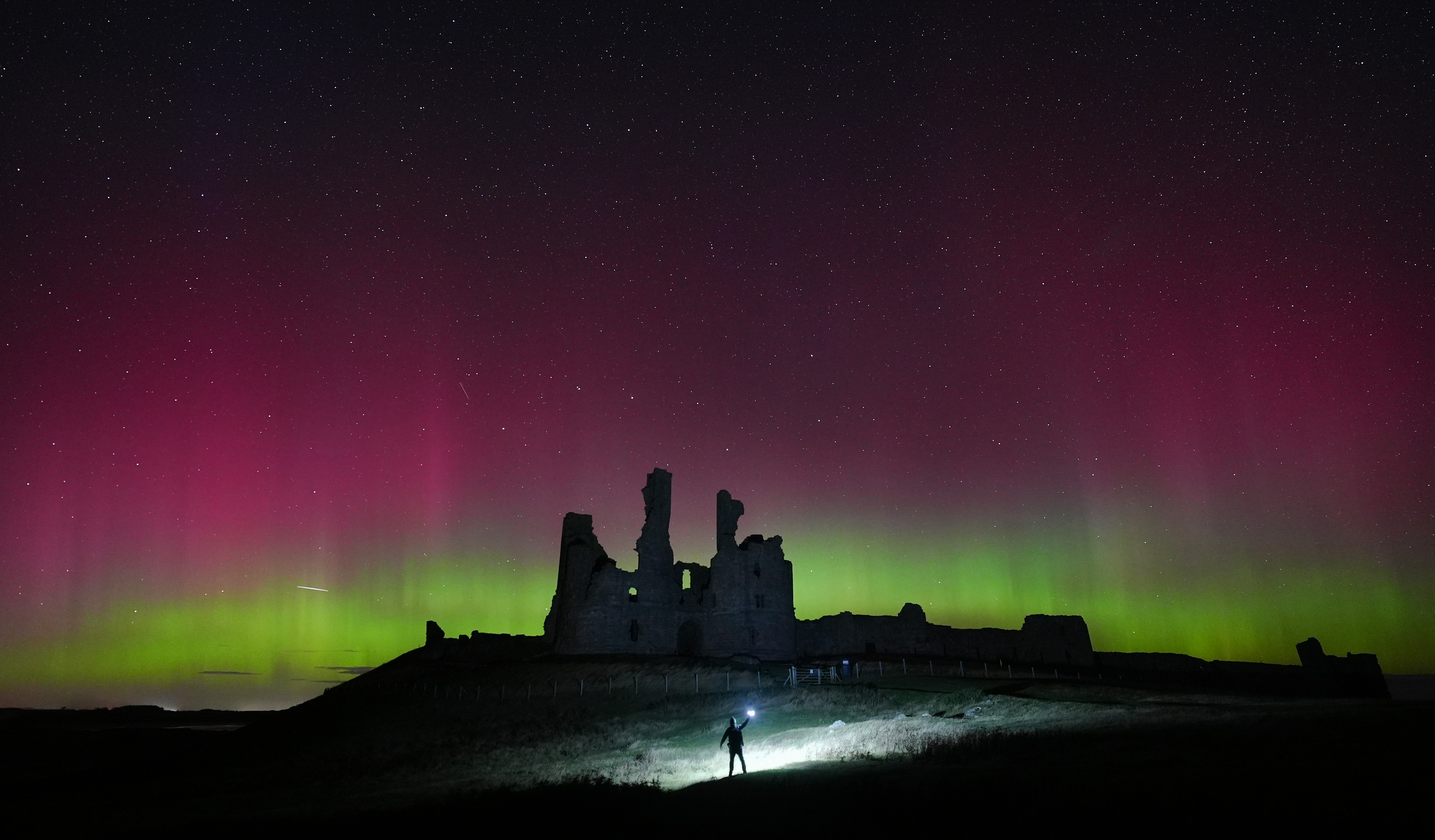 The Northern Lights light up the sky above the ruins of a castle.