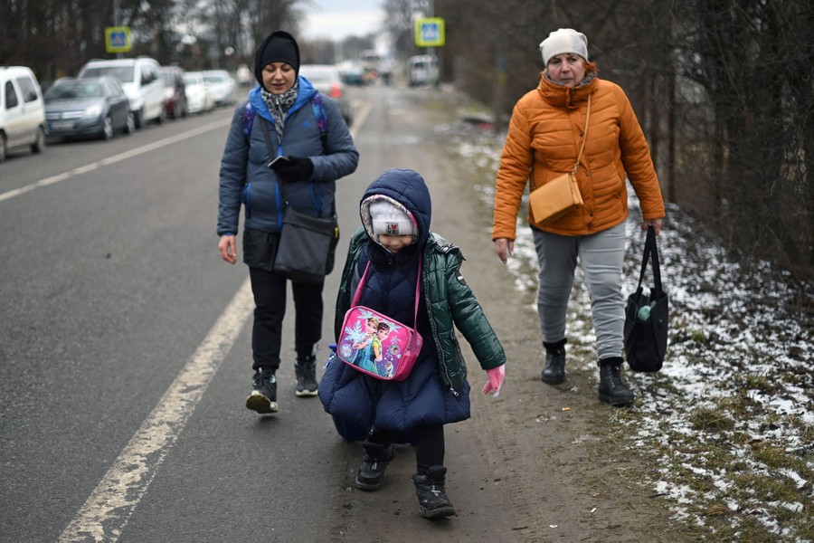 A child pulls along a suitcase, followed closely by two adults walking on the side of a two-lane highway.