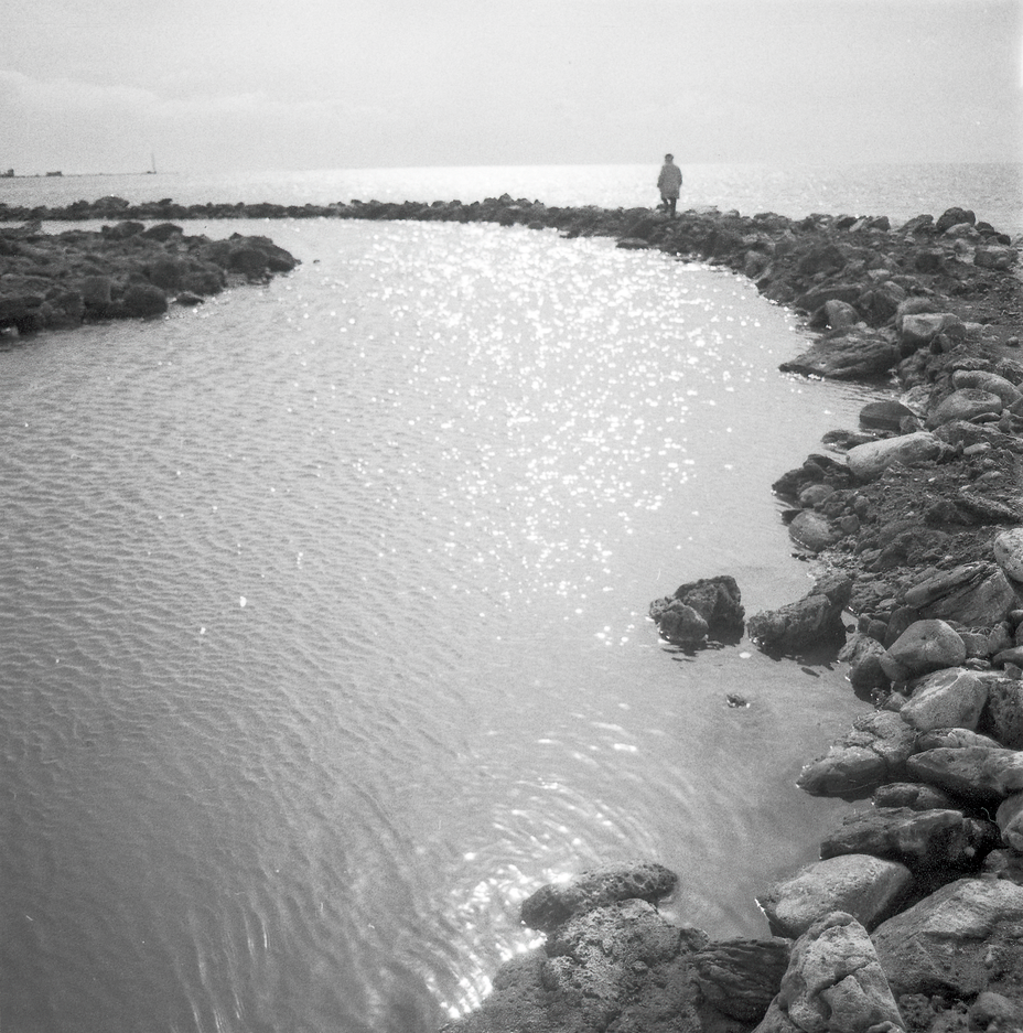 black-and-white photo of person walking along rocky path of spiral with lake in background