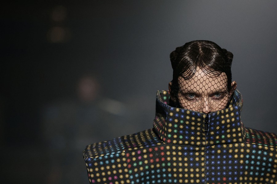 A model wears an oversize boxy garment and netting over their head and face.