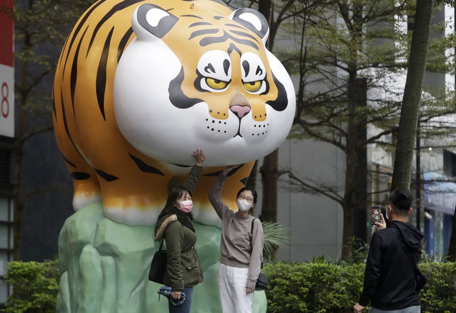 People pose with a round, cartoonish sculpture of a tiger.