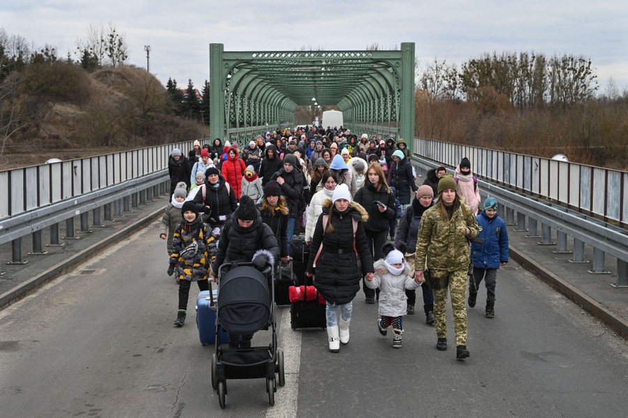 A large crowd of mostly women and children walk across a two-lane road bridge.