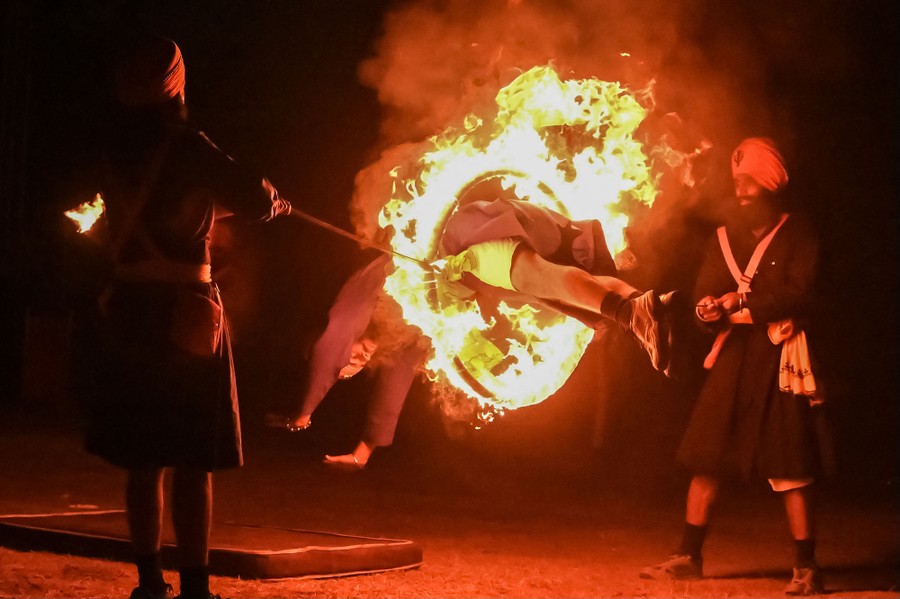 Two men hold a flaming hoop as another man dives through it.