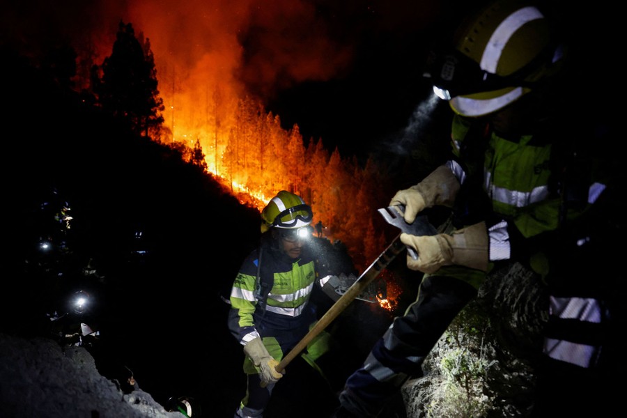 Several firefighters work at night on a steep hillside near a wildfire