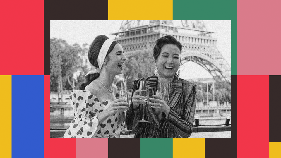 Lily Collins as Emily Cooper in "Emily in Paris" laughs with a friend while drinking champagne in front of the Eiffel Tower.