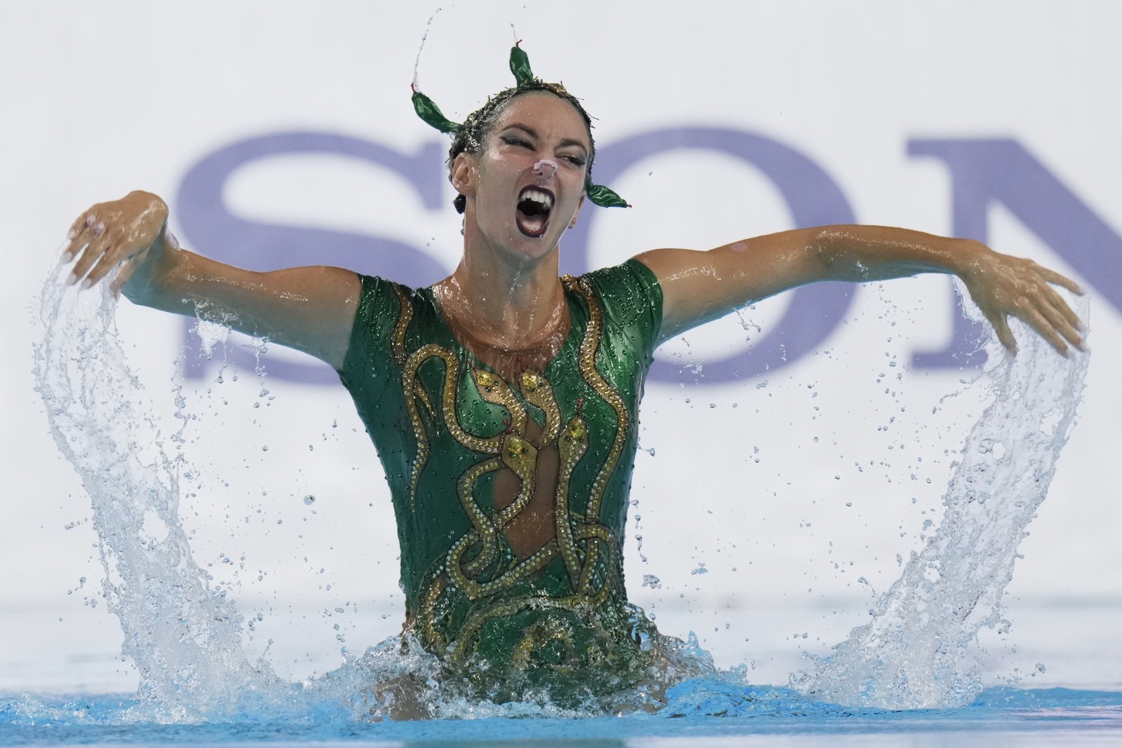 An artistic swimmer splashes and makes a fierce face during a performance.