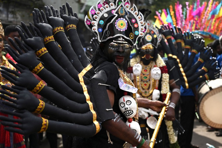 People wearing many-armed costumes parade in a street.