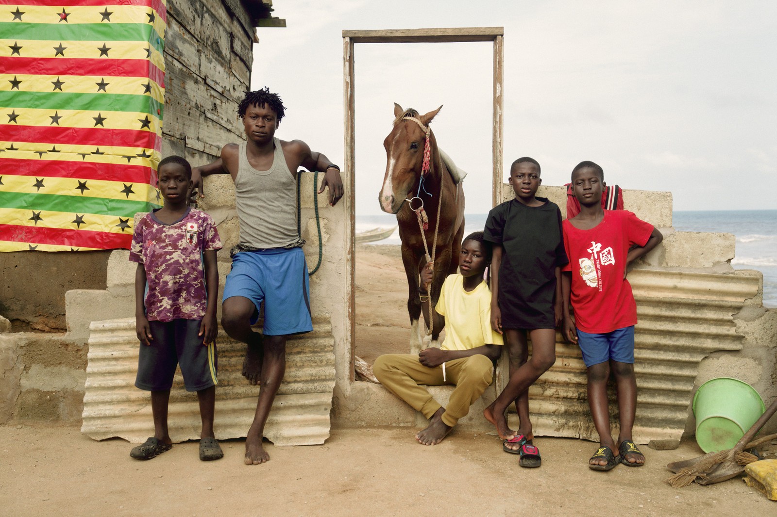 Five boys and young men pose outside a building beside a horse.