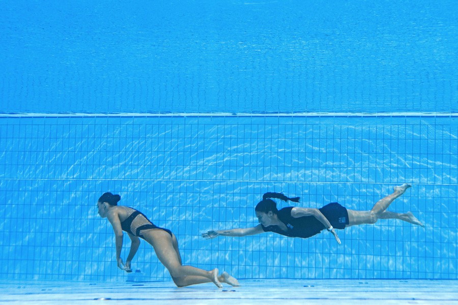 A woman swims underwater toward an unconscious swimmer at the bottom of a pool.