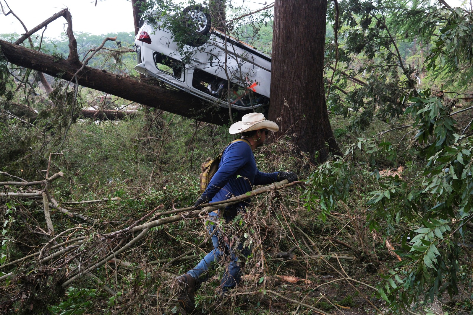 A person moves a downed tree branch, amid an overturned car and other flood debris.