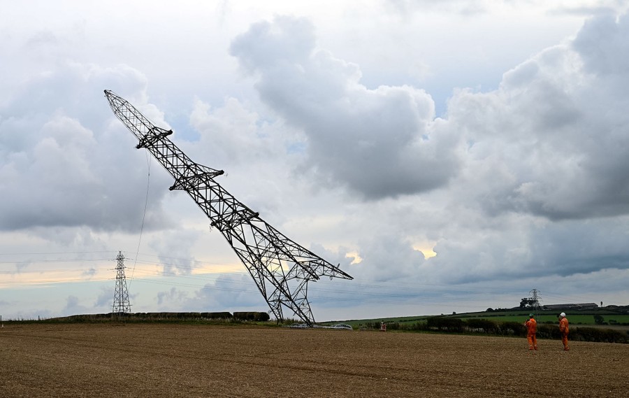 A large power pylon is tipped over, falling onto a field.