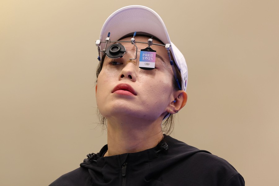 An Olympic pistol shooter prepares to compete, head tilted back, wearing complex eye gear, including a blind and a single lens.