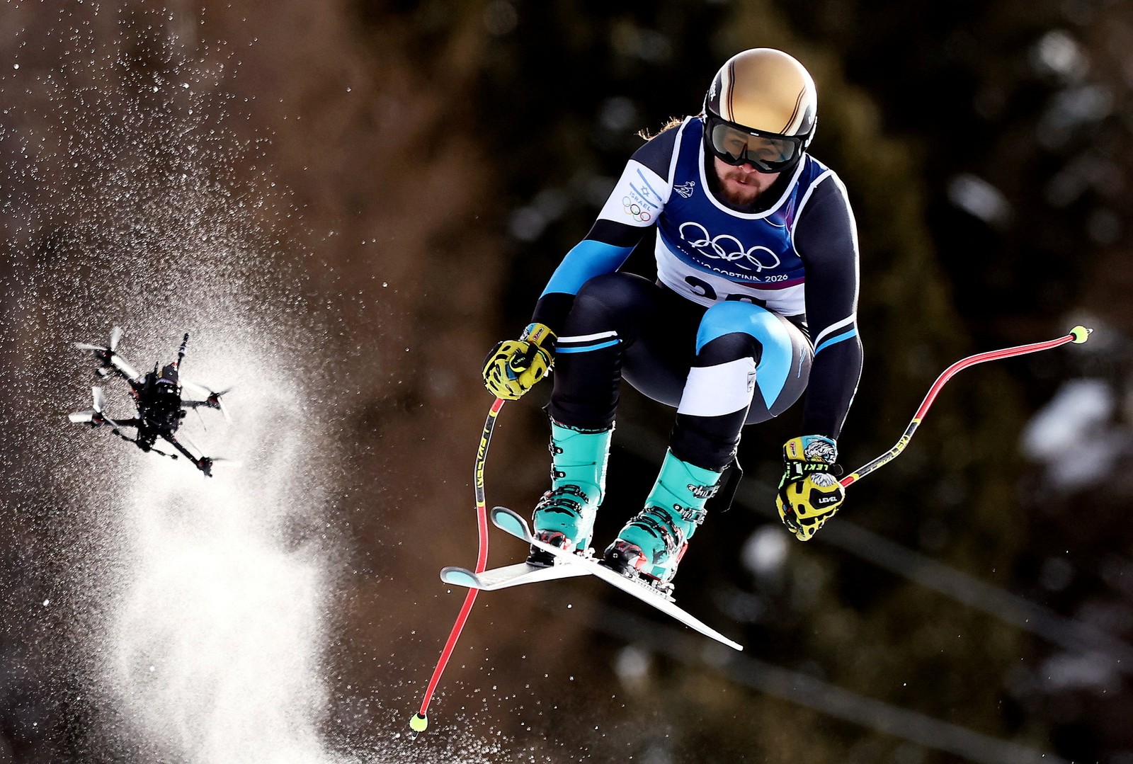 A skier catches some air during a downhill race, followed closely by a camera drone.