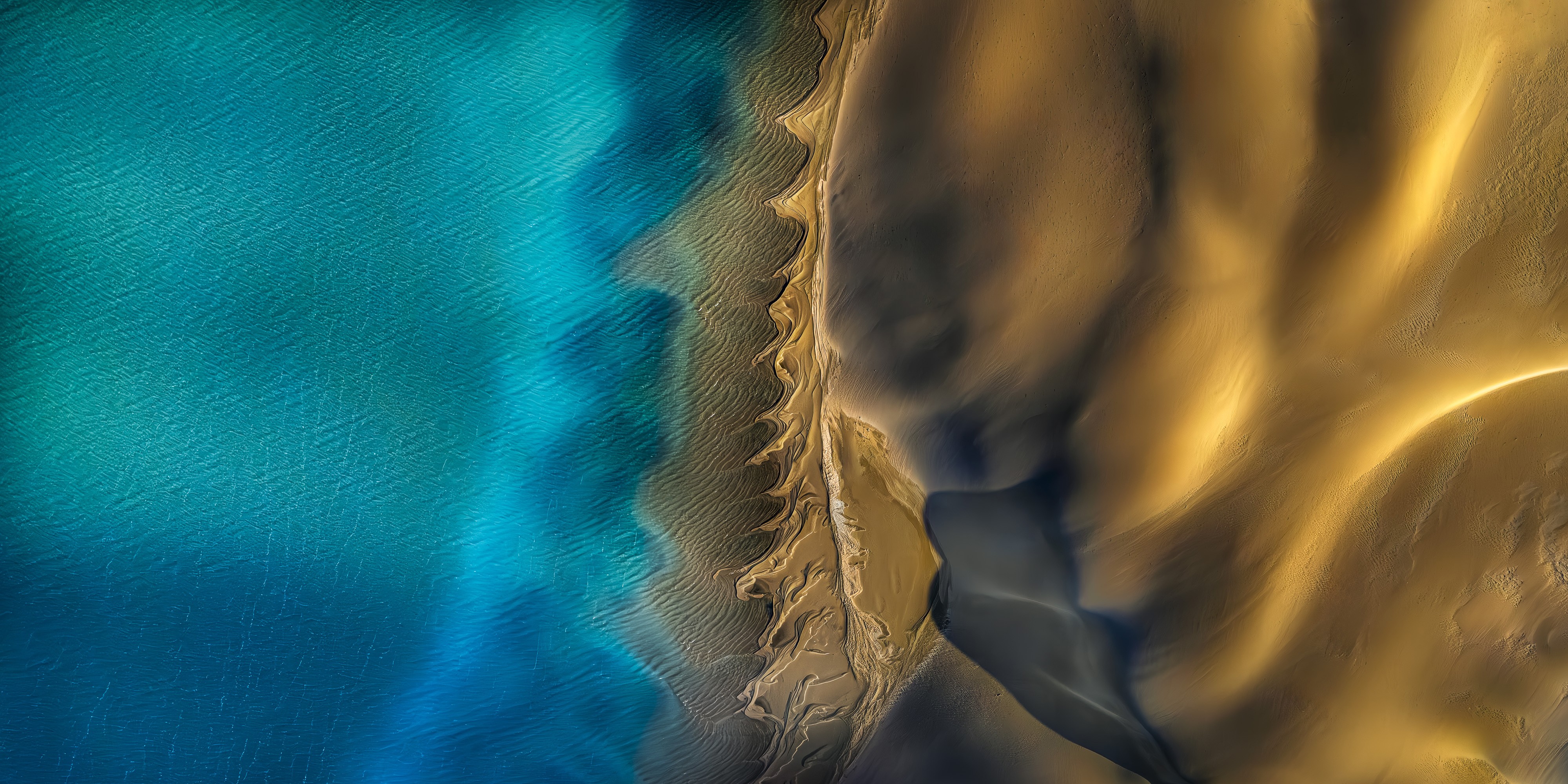 A drone's-eye-view of a sandy coastline beside a blue-green bay.