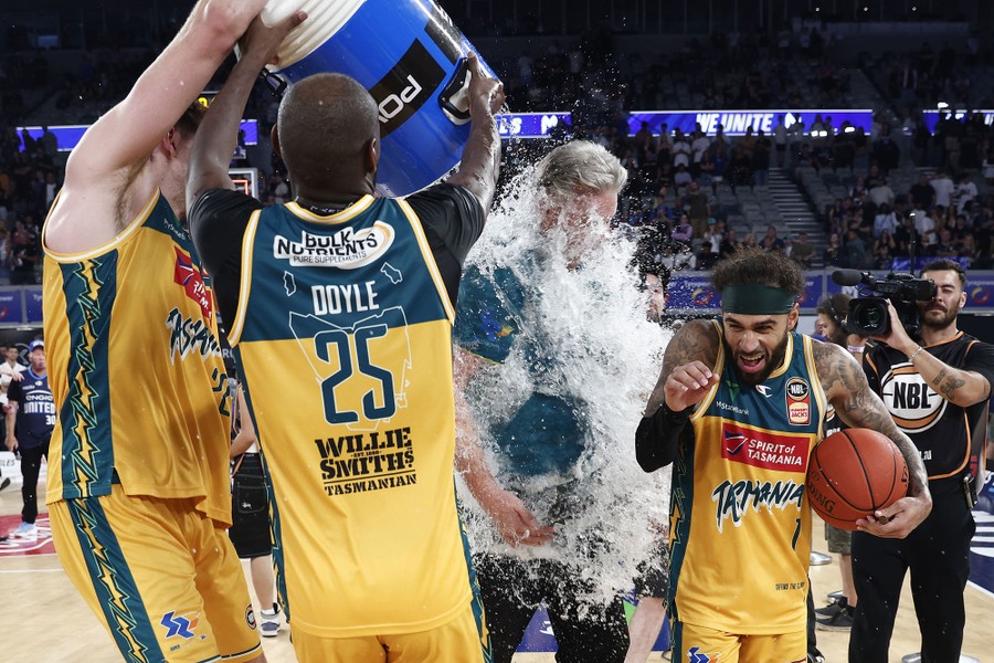 Two basketball players dump a bucket of water over their coach after winning a game.