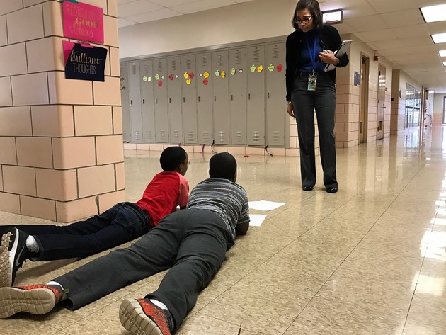 A principal looks over two students sprawled out on the floor of a hallway.