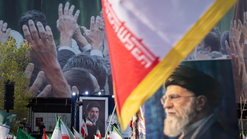 A color photo showing portraits of Ayatollah Ali Khamenei displayed alongside Iranian flags at a rally.