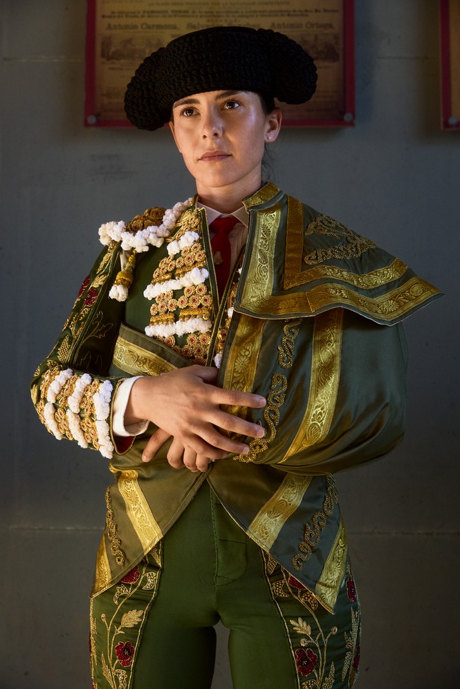 photo of woman wearing ornate green, gold, and white bullfighting jacket and pants with black hat
