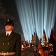 A soldier in a dress uniform stands guard in front of decorated military gravestones and a light display.