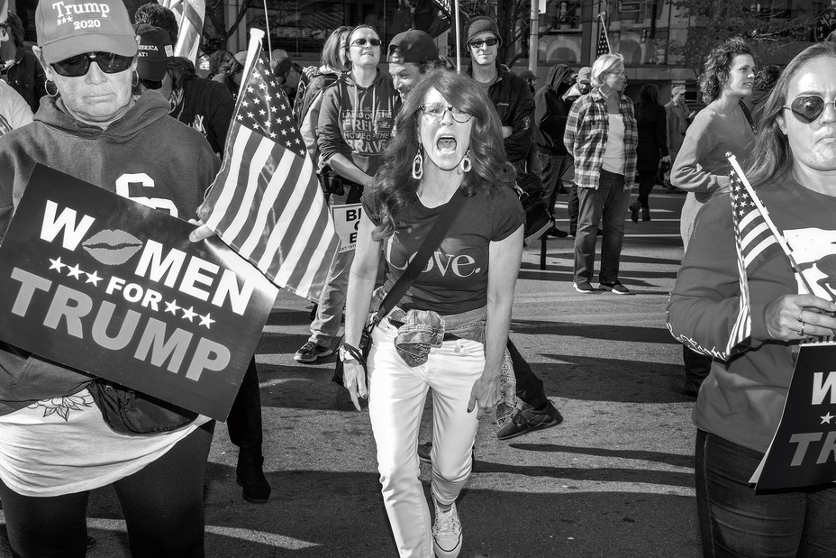 photo of woman in "Love" t-shirt screaming at rally, flanked by two people holding "Women for Trump" signs and American flags