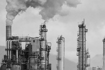 Smoke stacks at an oil refinery are shown against a gray sky