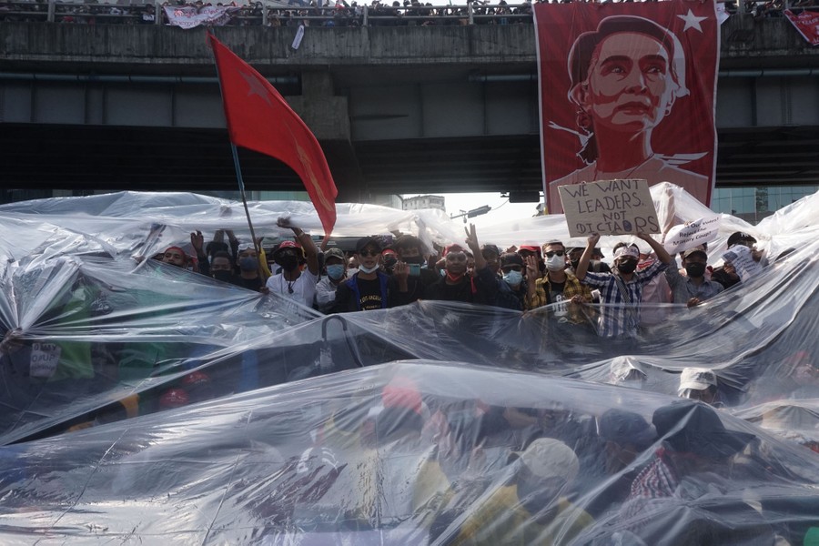 Dozens of protesters gather together carrying signs and flags beneath clear plastic fabric.