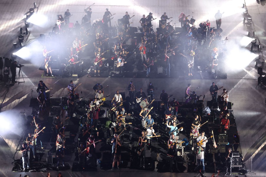Dozens of musicians stand in rows together, performing.