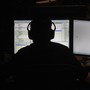 A person wearing headphones in silhouette, backlit by the light of two computer screens with code