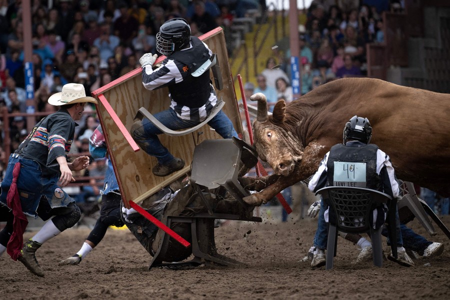 Several people wearing helmets scatter as a bull crashes into them in a rodeo stadium.