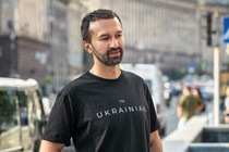 photo of man wearing "I'm Ukrainian" t-shirt, leaning against wall with busy city street in background