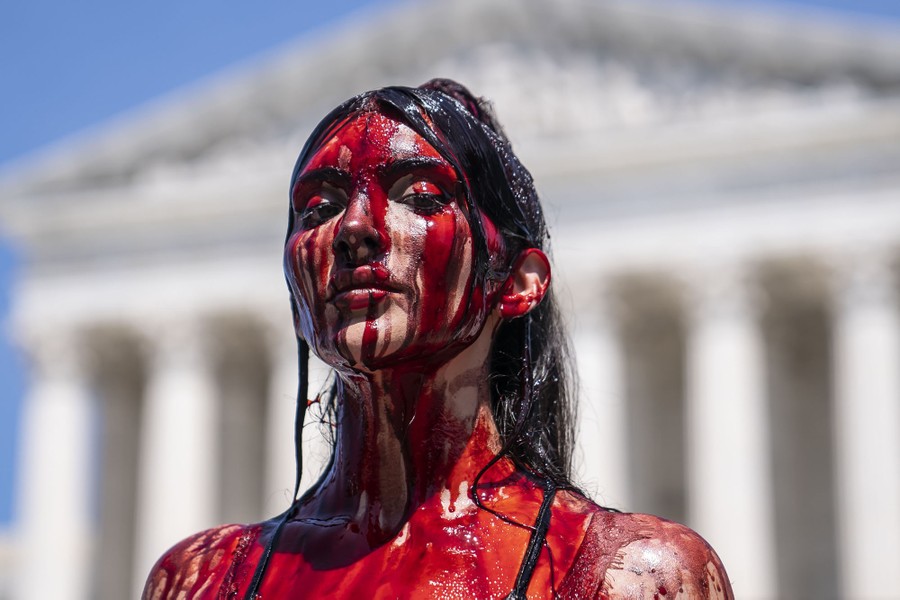A protester covered in fake blood stands in front of the U.S. Supreme Court building.