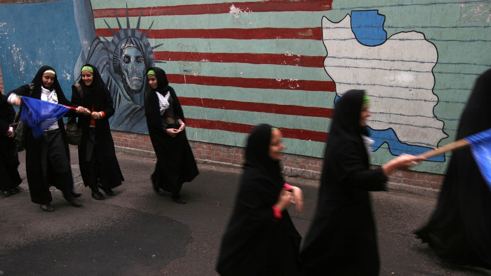 Iranian students walk past an anti-American mural, the Statue of Liberty with skull head and Iran's map.
