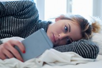 A woman stares at her phone in bed.