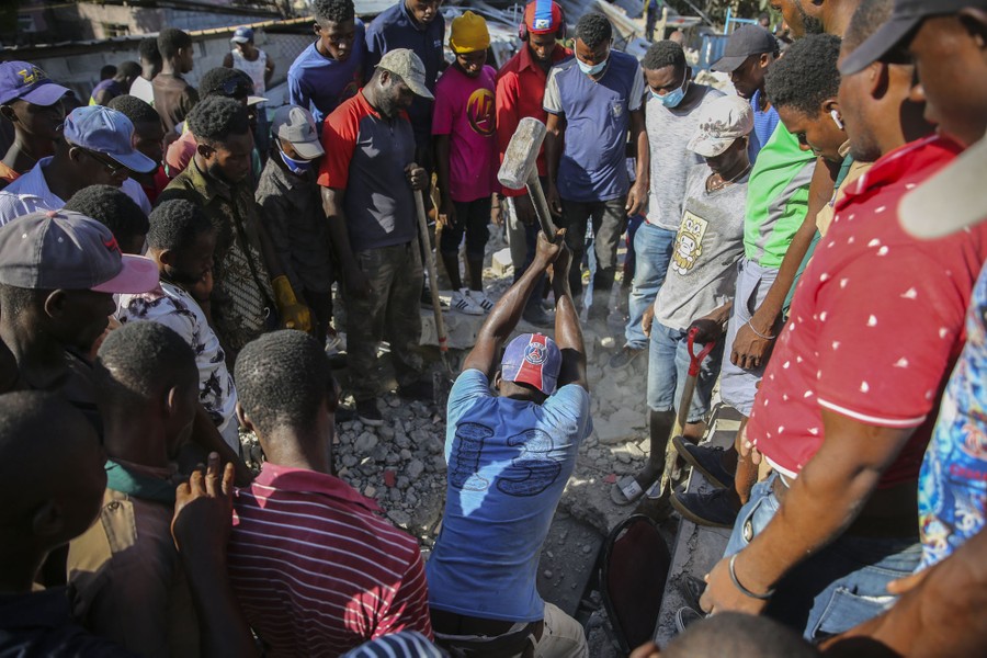 A man uses a sledgehammer to try to rescue people from the rubble of a home destroyed by the earthquake in Les Cayes.