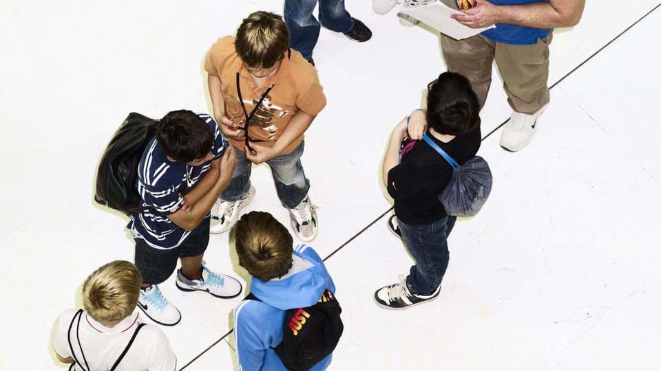 A color photograph of a group of young students seen from above, talking and wearing backpacks.