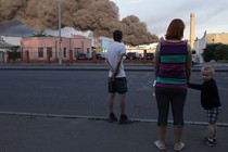 People observe a cloud of smoke from a fire in the background after a missile strike