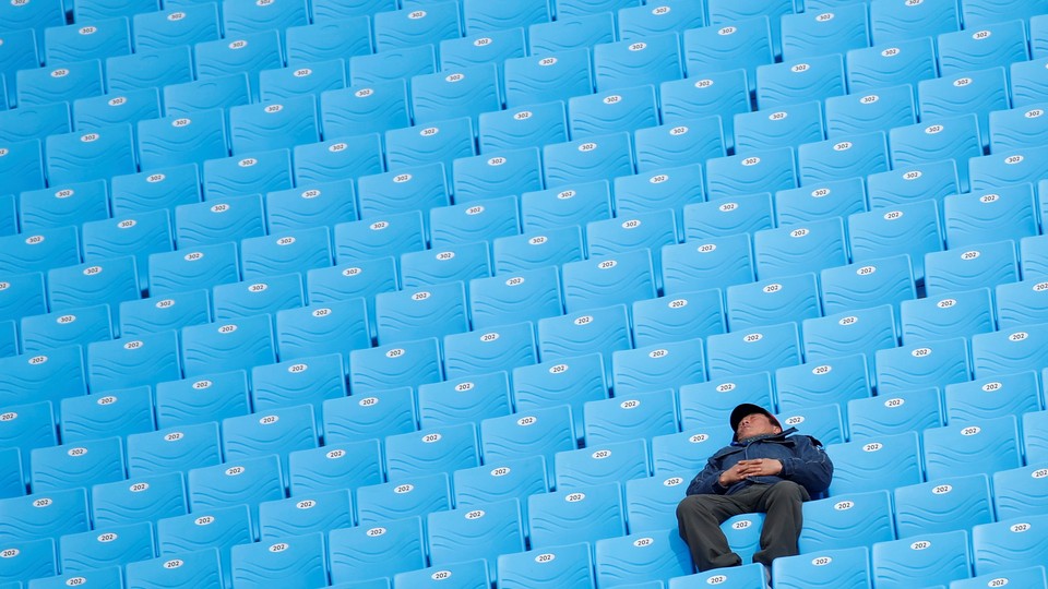 A man naps in a row of empty, bright-blue chairs.