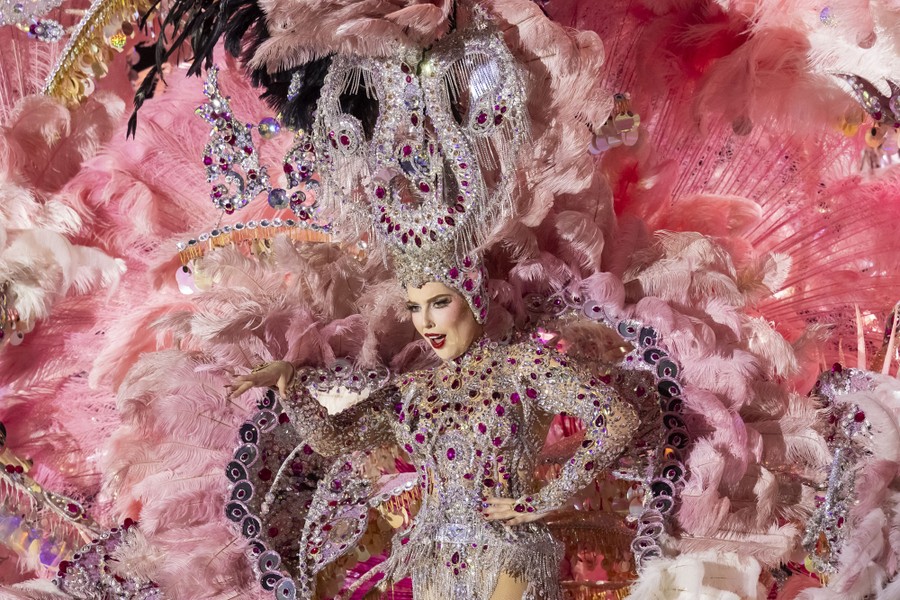 A performer poses while wearing a huge and ornate costume made of feathers, fabric, jewels, and more.