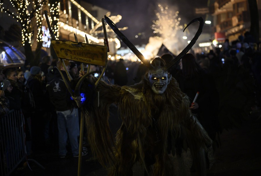 Performers wearing frightening Krampus costumes walk past a crowd during a parade at night.