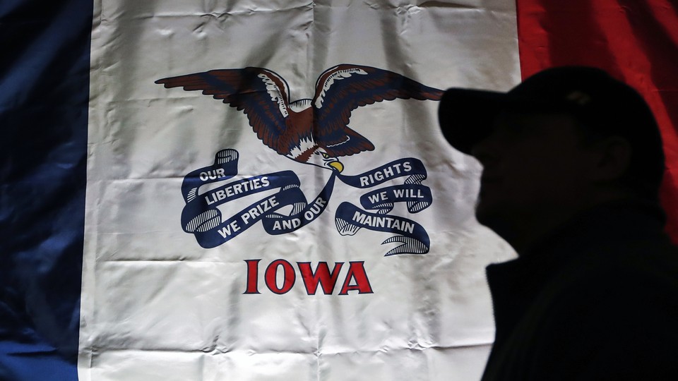 The Iowa state flag hangs at a rally site at the University of Iowa in Iowa City. A person, in shadow and wearing a baseball cap, stands in front of it.