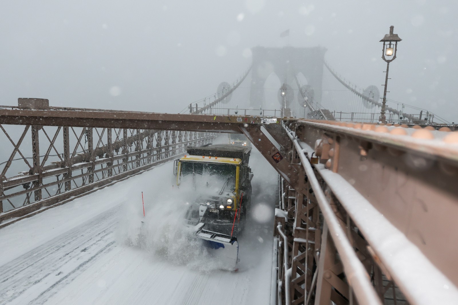 A snowplow drives across a bridge during a snowstorm.