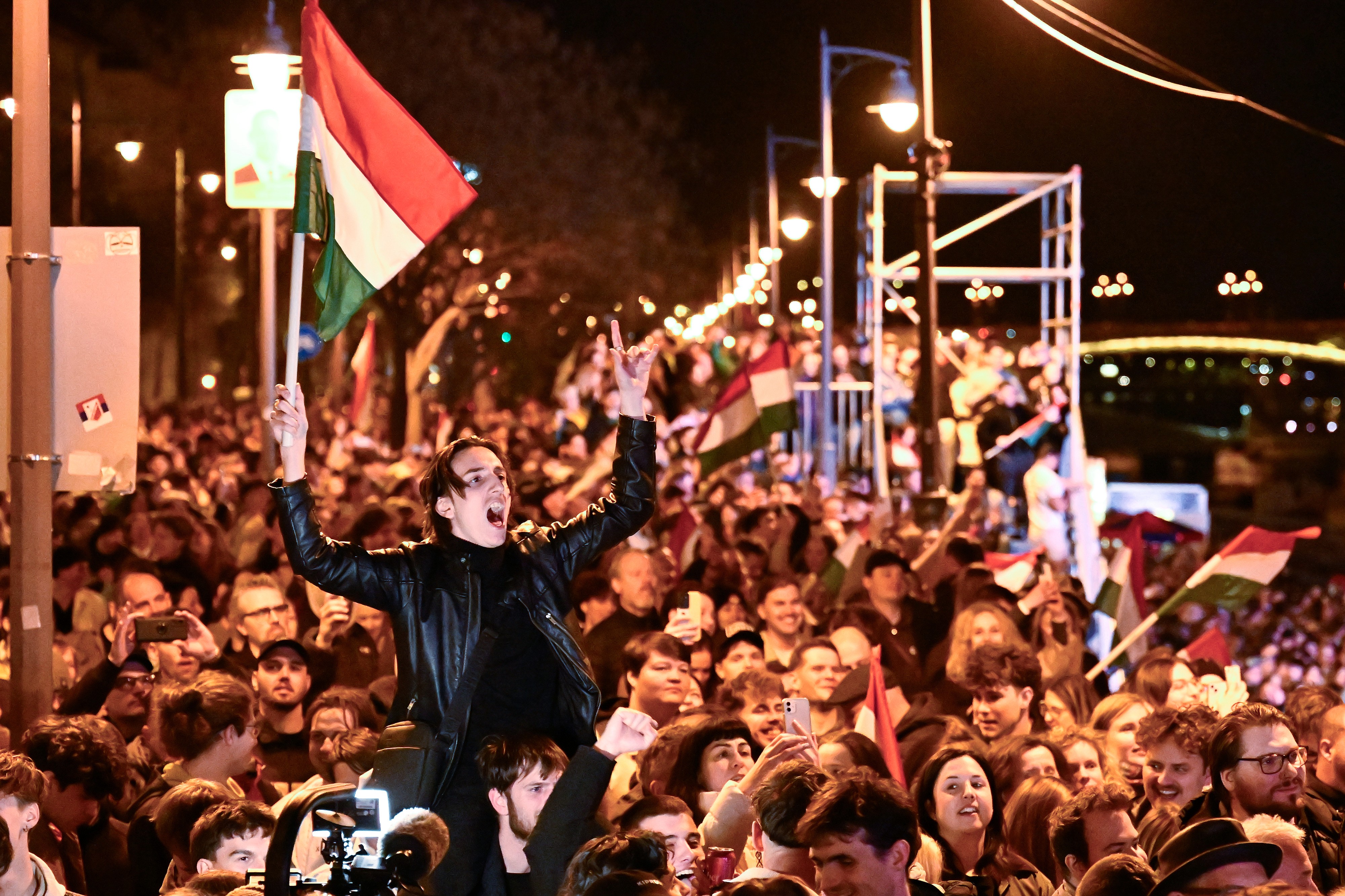 A man waves a Hungarian flag as he celebrates among a large crowd.