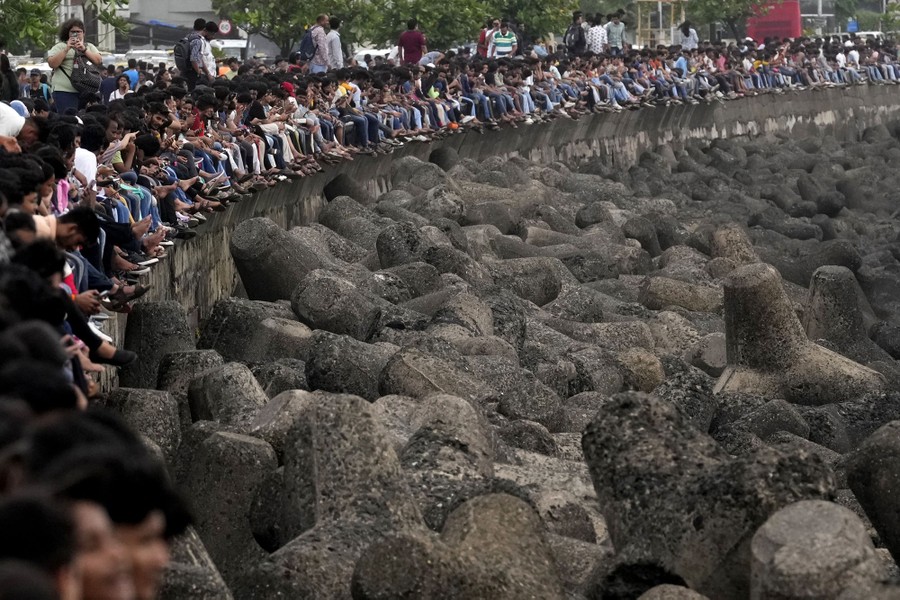 Dozens of people sit along a seawall overlooking piles of wave-dissipating concrete blocks.
