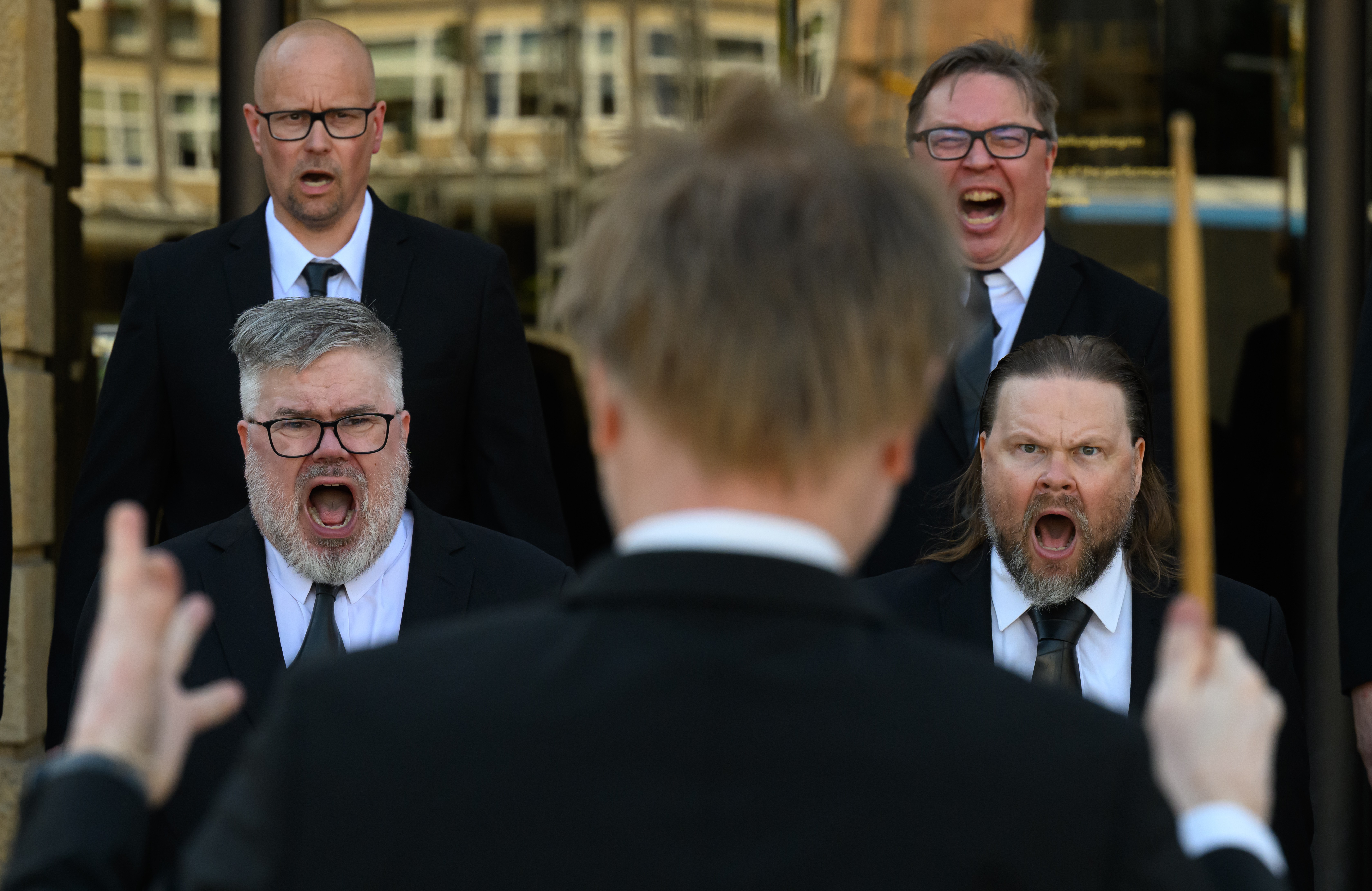 A person conducts a choir of shouting men.
