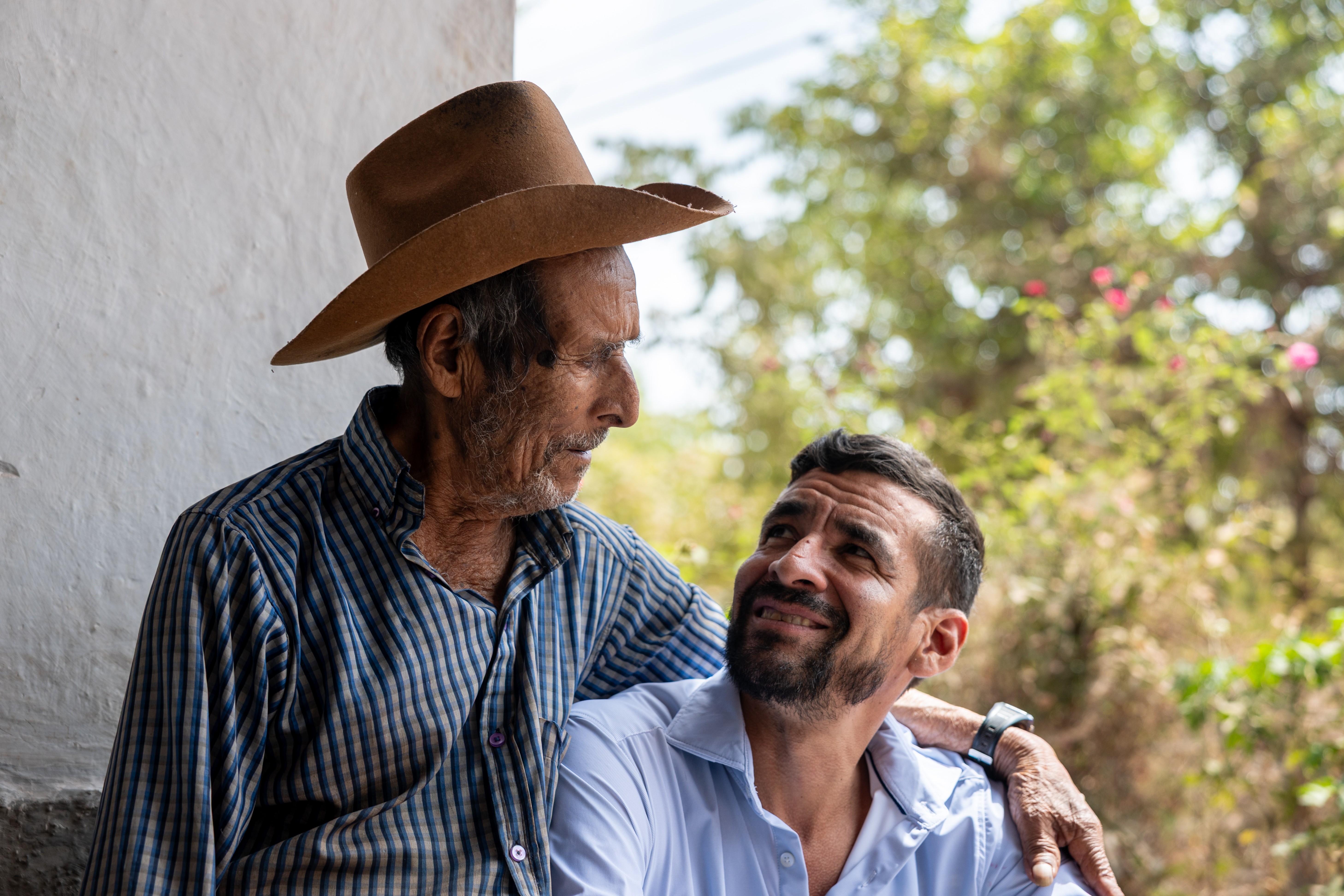 An elderly man sits beside his grandson, embracing him.