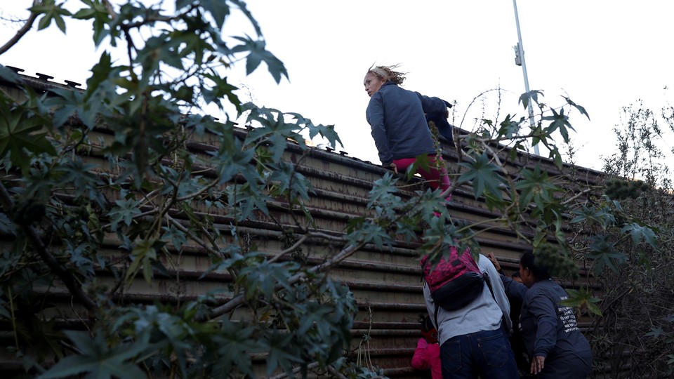 Migrants try to jump over the border wall to cross from Mexico to the U.S. on December 15, 2018.